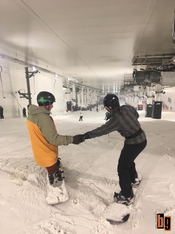 Swifty supporting a beginner by holding their hands while boarding